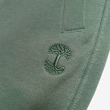 Detailed close of embroidered Oaklandish tree logo under the front pocket of army green joggers.