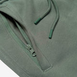 Detail close up of of army standard sweatpants front zippered pocket and drawcords with metal tips.