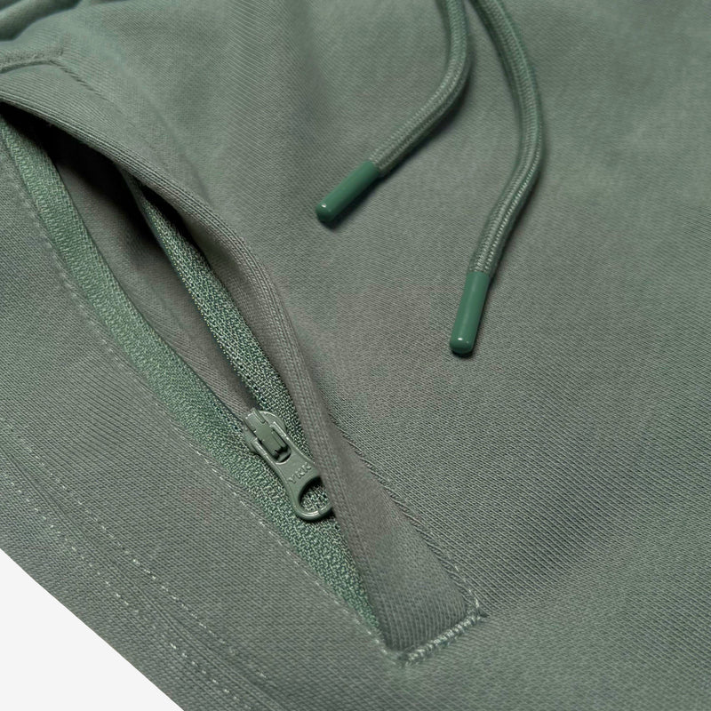 Detail close up of of army standard sweatpants front zippered pocket and drawcords with metal tips.