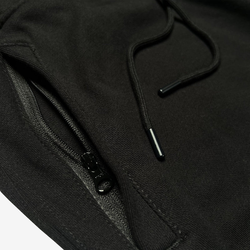 Detail close-up of front zippered pocket and drawcords with metal tips on black Oaklandish joggers.