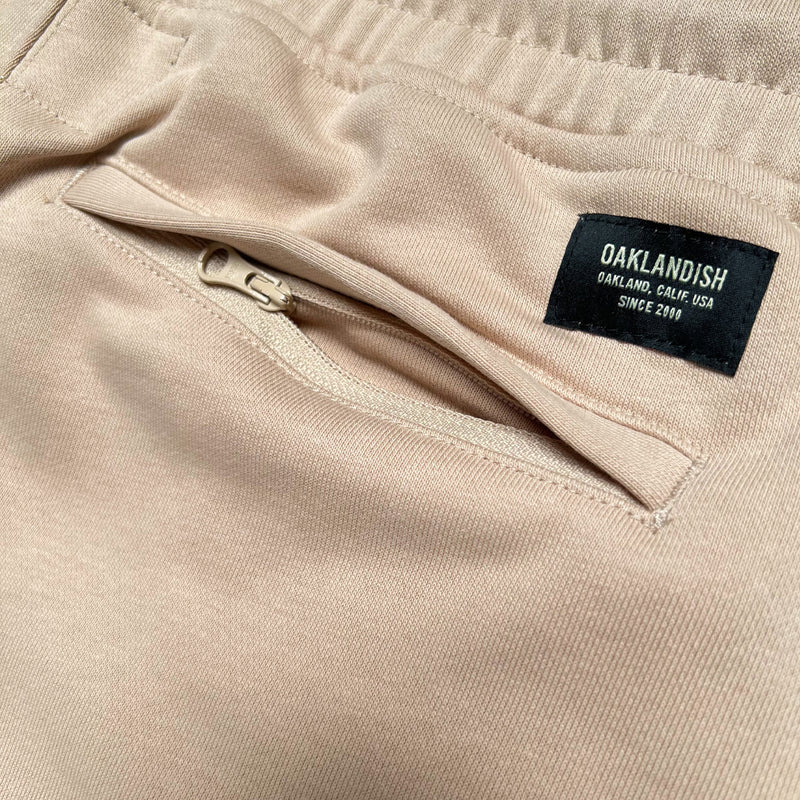 Detail close-up of the Oaklandish label above the back zipper pocket of sand-colored joggers.