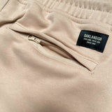 Detail close up of sand standard sweatpants woven label above right back zipper pocket.