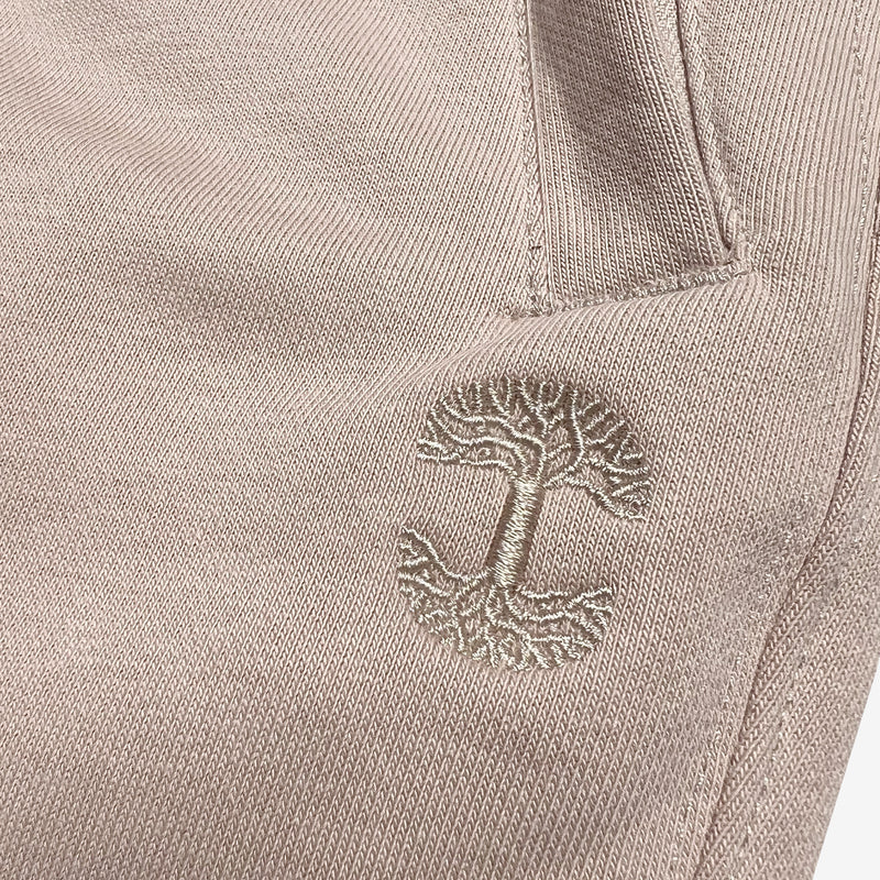 Detailed close of embroidered Oaklandish tree logo under the front pocket of sand-colored joggers.