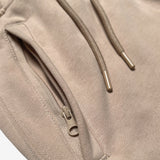 Detail close up of of sand standard sweatpants front zippered pocket and drawcords with metal tips.