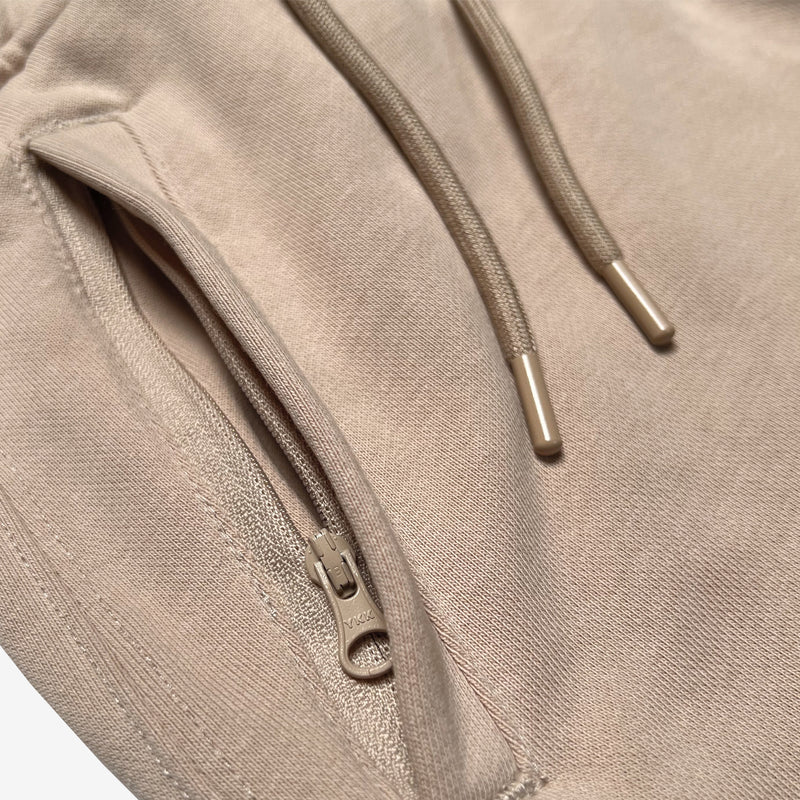 Detail close-up of front zippered pocket and drawcords with metal tips on sand-colored Oaklandish joggers.