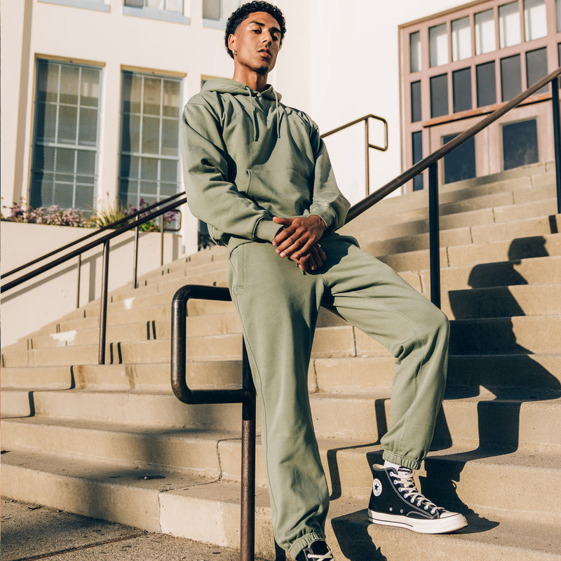 Male model outside wearing a sweatsuit hoodie and jogger set with Oaklandish logos, wordmarks, and embroidery details across the chest.