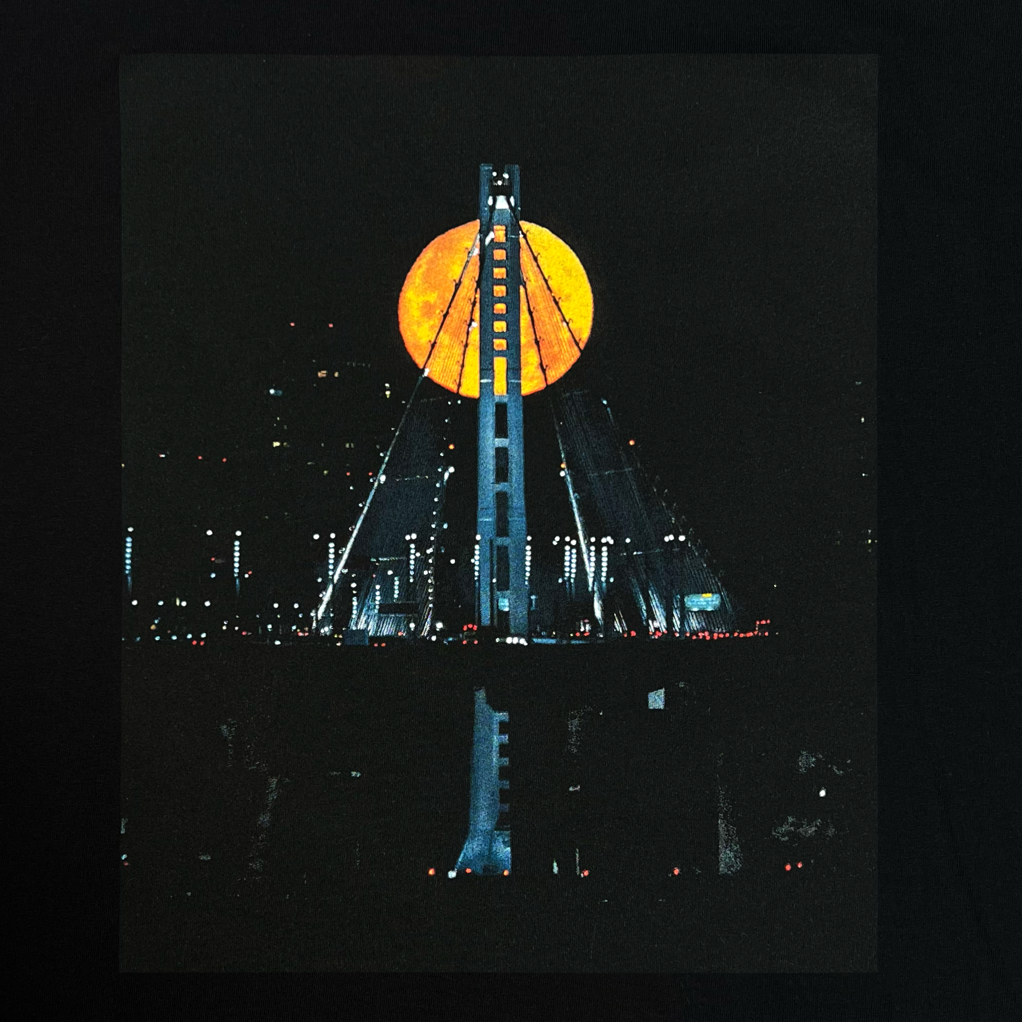 Close-up of the image of Strawberry Moon over the Oakland bridge by landscape photographer Vincent James on a blackl cotton t-shirt.