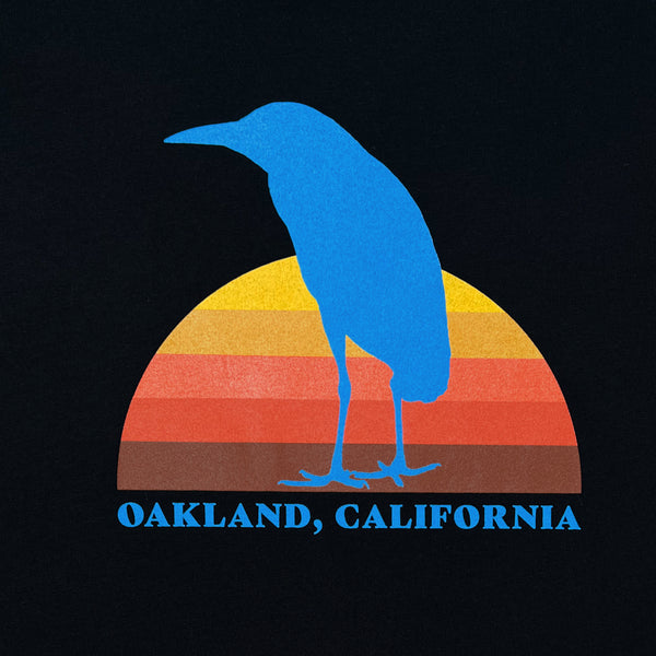 Close up detail image of Sun Heron graphic & Oakland California wordmark on black cropped women's tee.