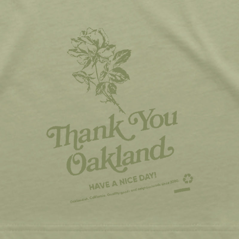 Close up of green graphic with a flower and the words “Thank-You Oakland. Have a Nice Day” on a khaki women’s tee.