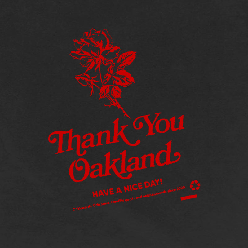 Close-up of the red graphic of a flower with the words “Thank-You Oakland. Have a Nice Day” on a black t-shirt.