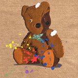Detailed close-up of artistically painted battered teddy bear with yellow and red paint splatter on a brown t-shirt.