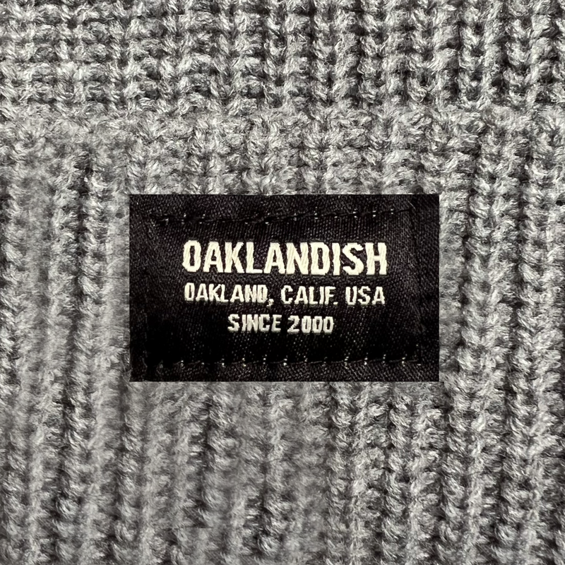 Close-up of Oaklandish square patch on the front cuff of an athletic heather grey ribbed knit beanie.