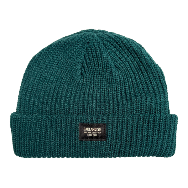  Close-up of Oaklandish square patch on the front cuff of a jade green ribbed knit beanie.