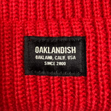 Detail close up of cuffed red short knit beanie with Oaklandish square patch.