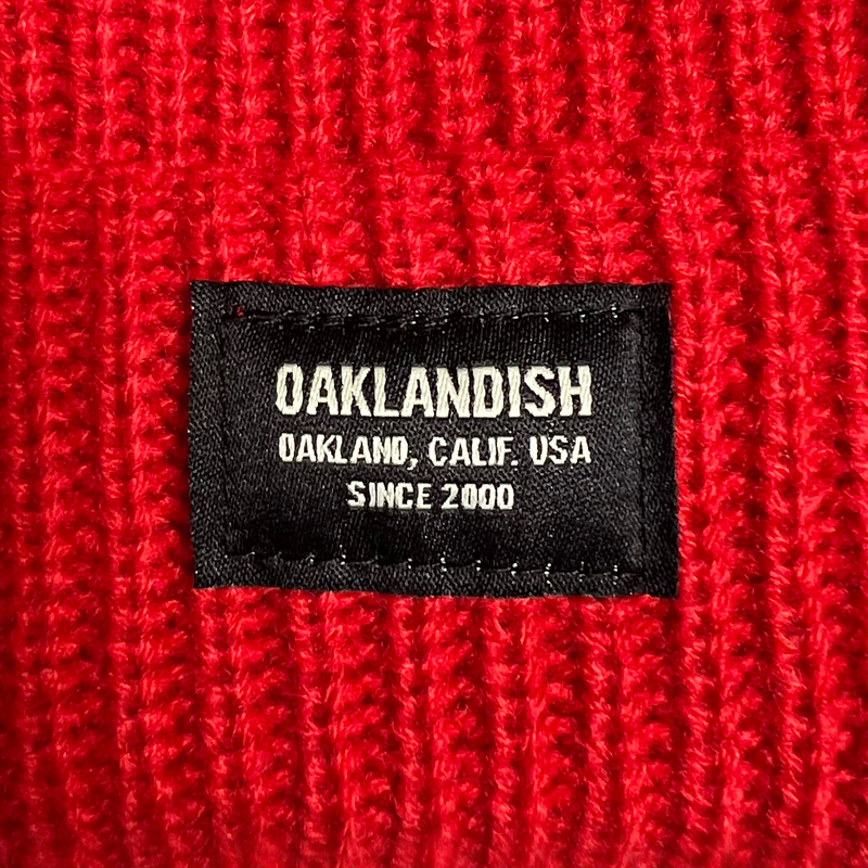 Detail close up of cuffed red short knit beanie with Oaklandish square patch.