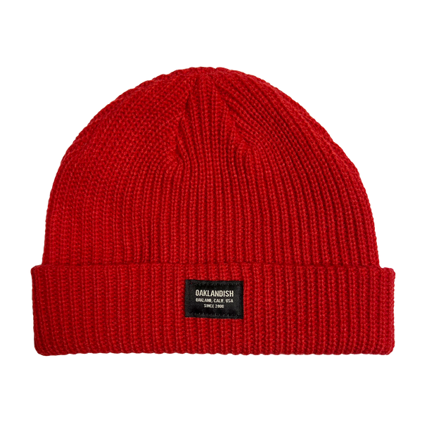Close-up of Oaklandish square patch on the front cuff of red ribbed knit beanie.
