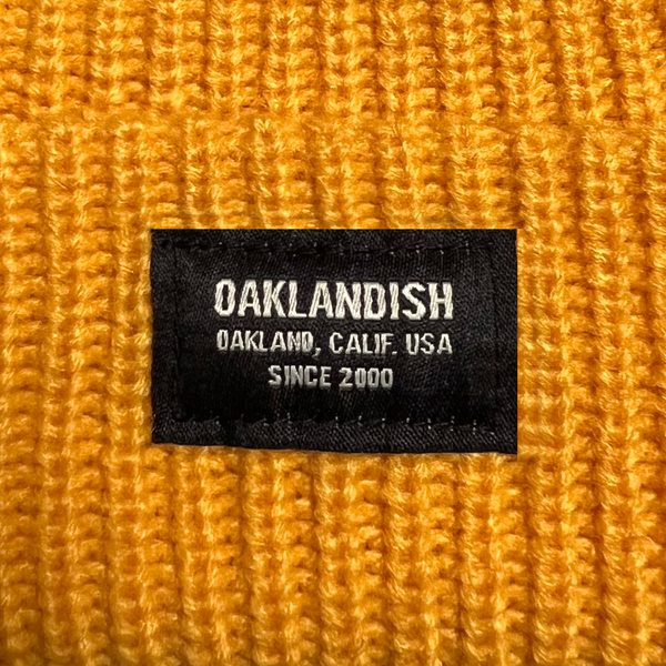 Close-up of Oaklandish square patch on the front cuff of a gold beanie.