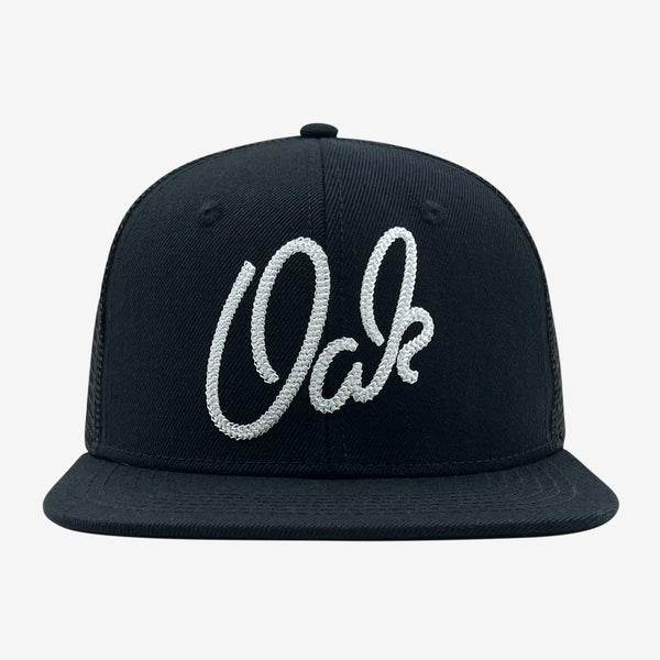 Black trucker cap with OAK wordmark embroidered in chain stitch on the crown.