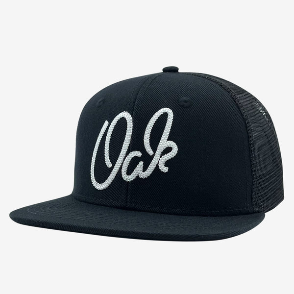 Black trucker cap with OAK wordmark embroidered in chain stitch on the crown.