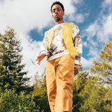 Man standing outdoors wearing wood duck all over print on cream crewneck Oaklandish logo sweatshirt.