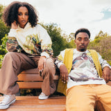Man and woman sitting outdoors wearing crewneck Oaklandish sweatshirts with wood duck all over print.
