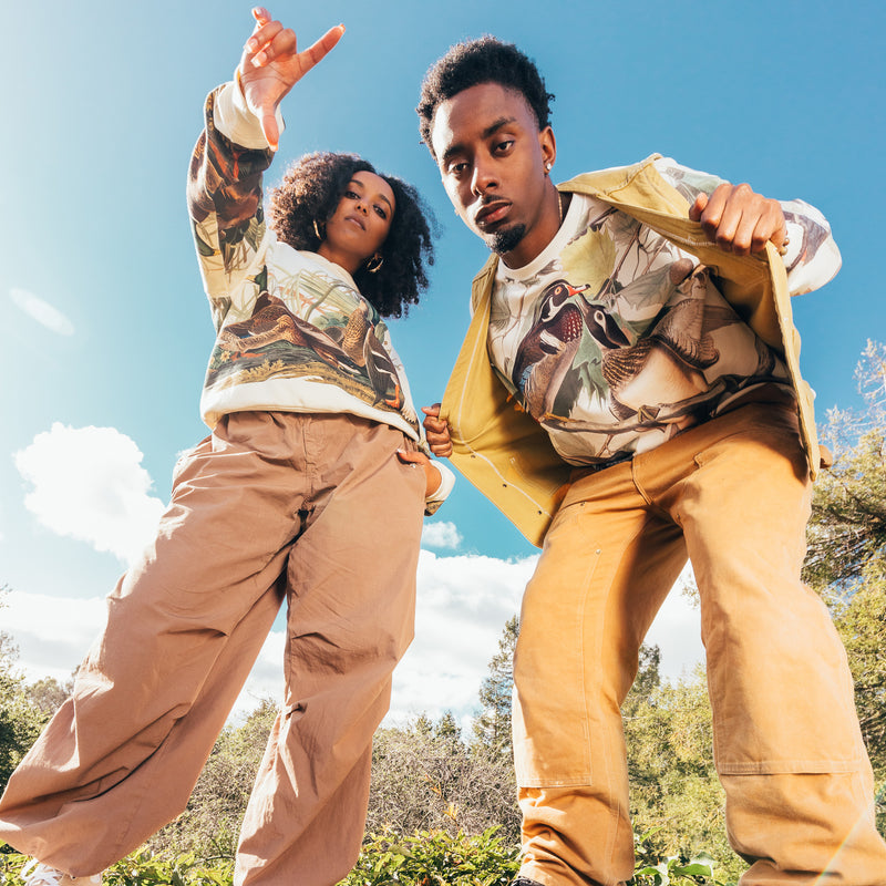 Man and woman wearing crewneck Oaklandish sweatshirts with wood duck all over print.