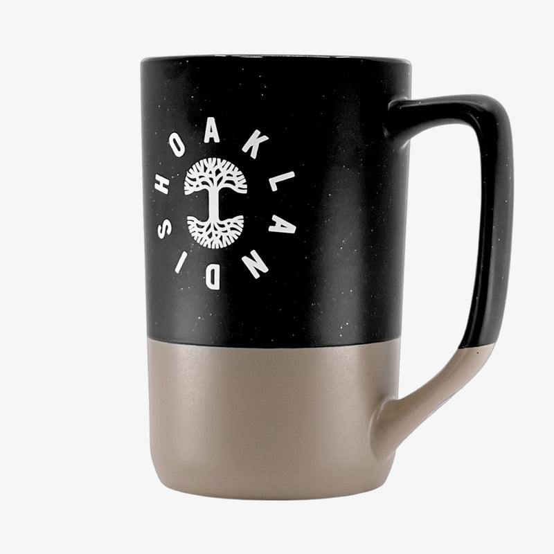 Side angle of the backside of a black and tan two-tone stoneware mug with the Oaklandish wordmark circling the Oaklandish tree logo.