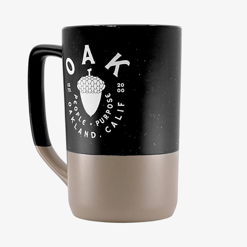Side angle of black and tan two-tone stoneware mug depicting an acorn with the words “OAK People, Purpose, Oakland Calif.”