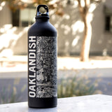 A black water bottle imprinted with an aerial Oakland map and Oakland wordmark, with screw top on an outdoor table.