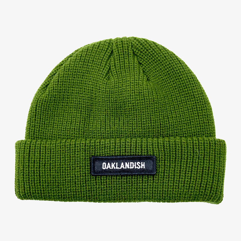 Green shorter style olive green cuff beanie with white Oaklandish wordmark on a black patch on the cuff.