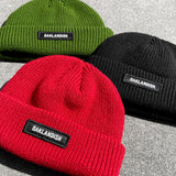 Olive green, black, and red cuffed Oaklandish beanies lying on asphalt outdoors.