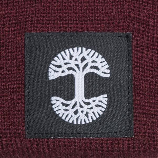 A close-up of the black and white Oaklandish logo tag on a burgundy woven beanie.