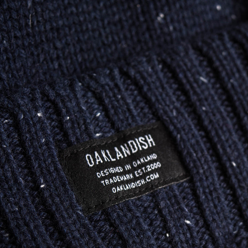 Close up of Oaklandish tag on the front cuff of a navy beanie with white flecks.