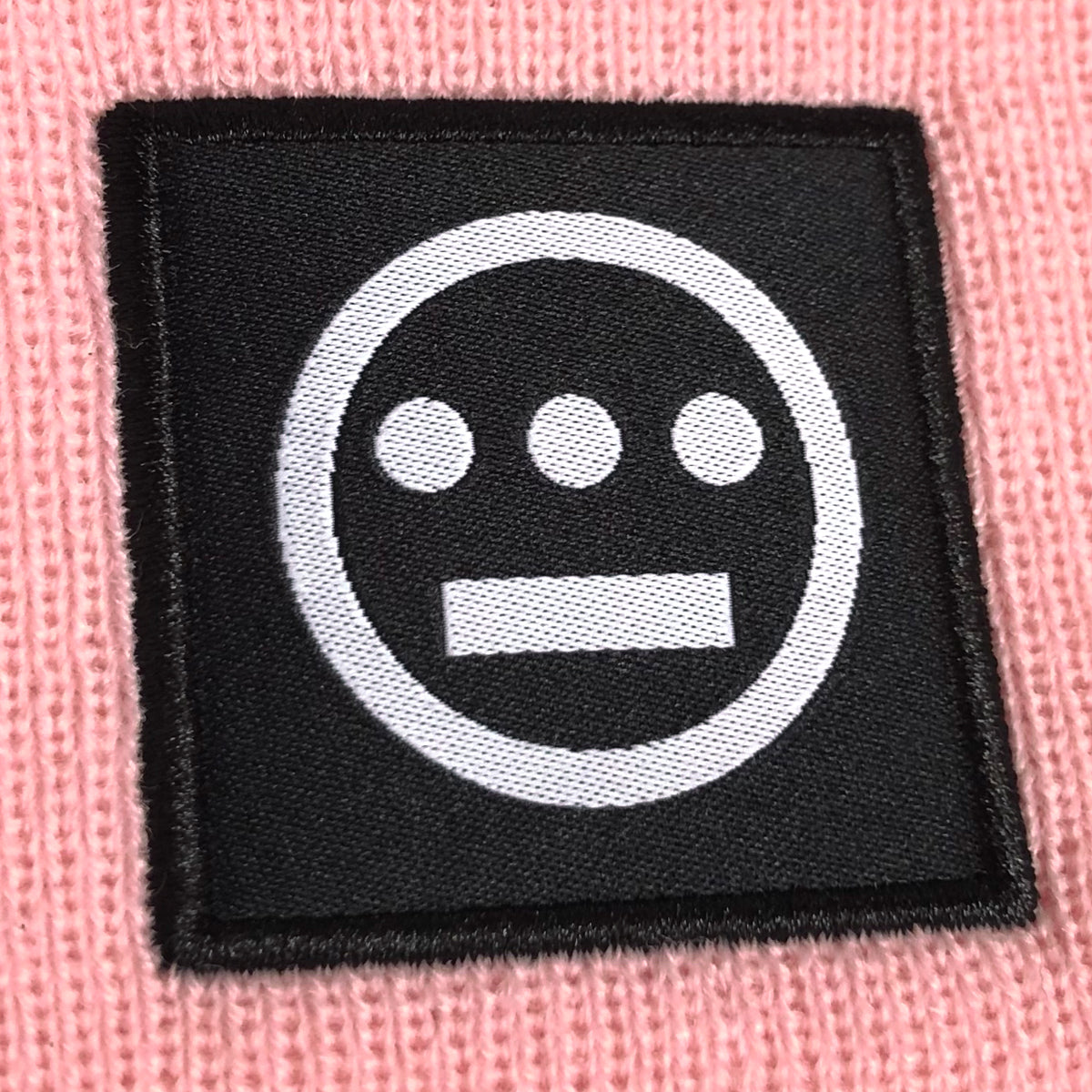 Close up of black and white hiero hip-hop logo patch on the cuff of a pink beanie.