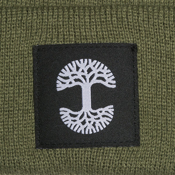 A close-up of the black and white Oaklandish logo tag on an olive green woven beanie.