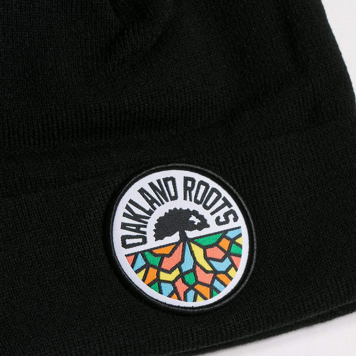 Close-up of full-color round Oakland Roots SC logo on the front cuff of a black cuffed beanie.