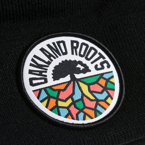Close-up of full-color round Oakland Roots SC logo on the front cuff of a black cuffed beanie.