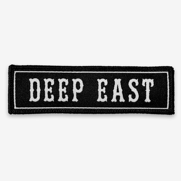 Black rectangle fabric iron patch, outlined with white line and capitalized word mark “DEEP EAST.”