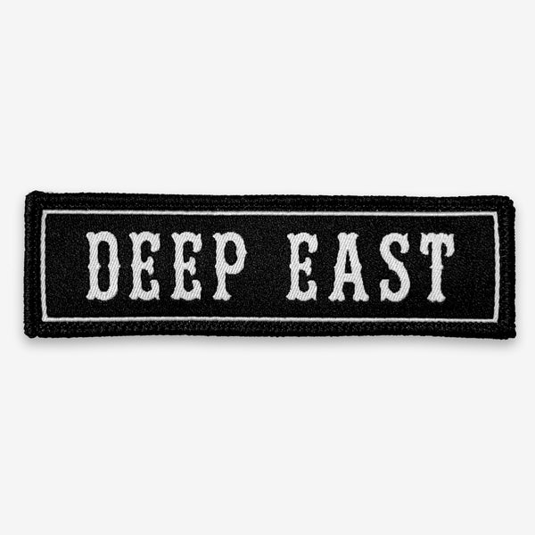 Black rectangle fabric iron patch, outlined with white line and capitalized word mark “DEEP EAST.”