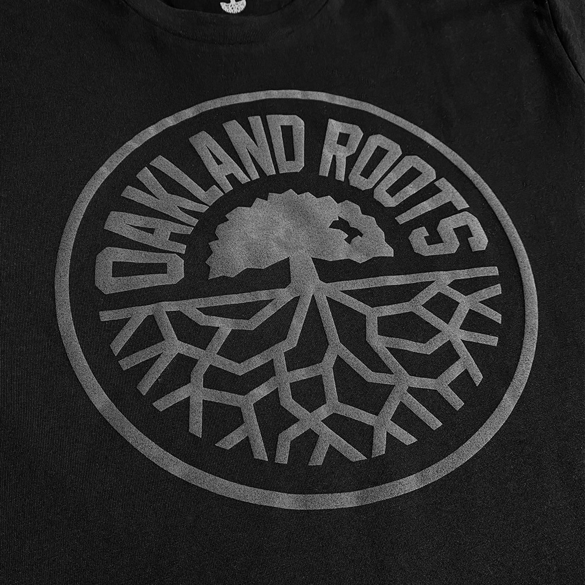 Close up of full circle black Roots SC logo on a black t-shirt.