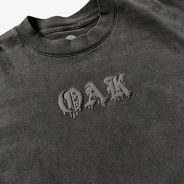 Close-up of OAK wordmark in old style font with a bleed on a vintage black t-shirt.  
