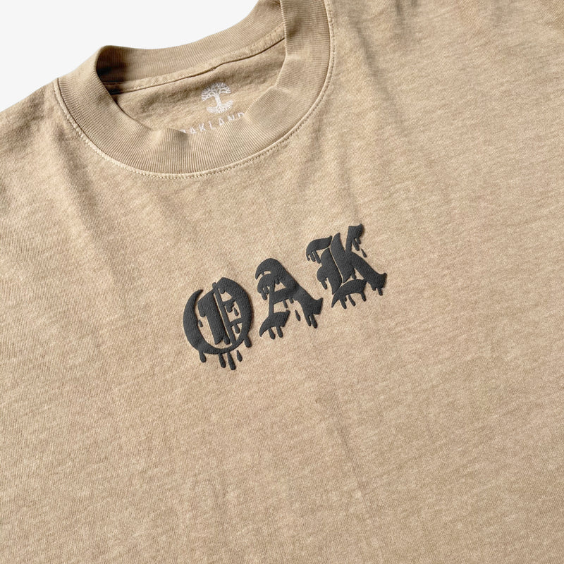 Close-up of OAK wordmark in old style font with a bleed on a mushroom brown t-shirt.  