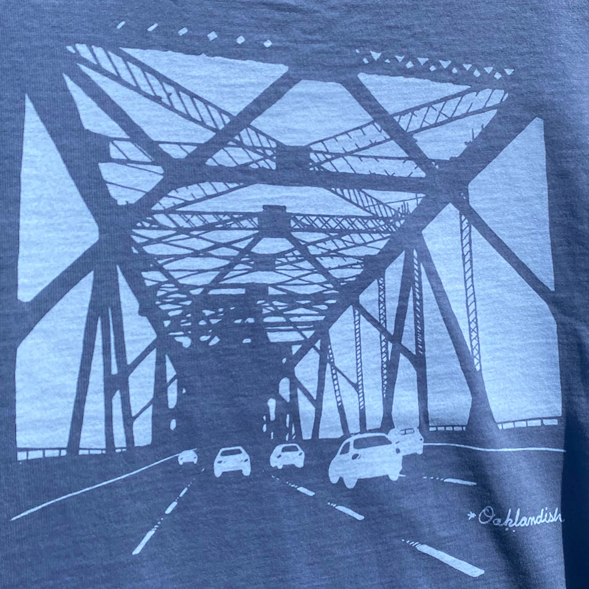 Close up of graphic of view from the eastern span of Oakland bridge on faded blue women’s t-shirt.