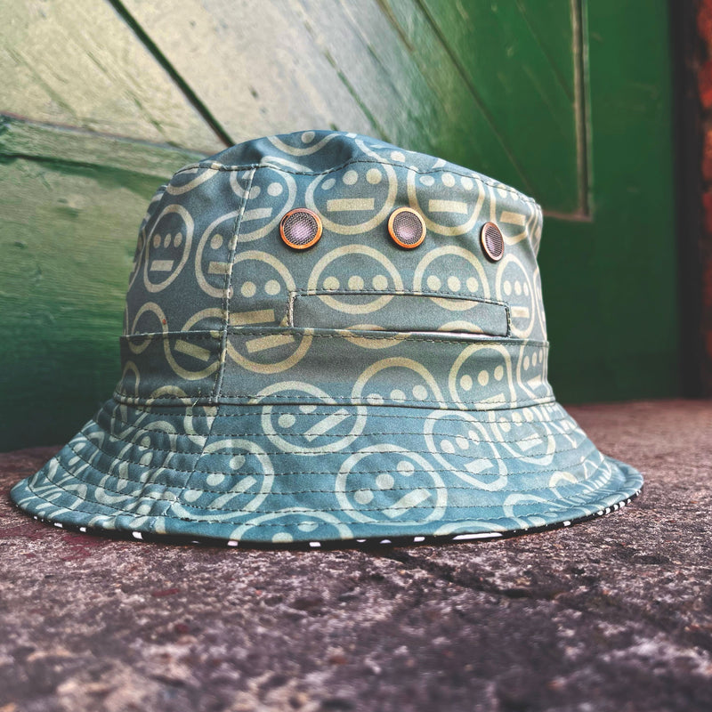 The green side of a reversible bucket hat with light green Hieroglyphics hip-hop logo on repeat sitting outdoors. 