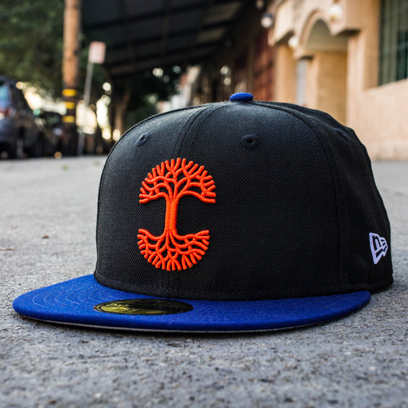 Side view of black New Era 59FIFTY black cap, with red embroidered Oaklandish logo and blue bill sitting on Oakland street.
