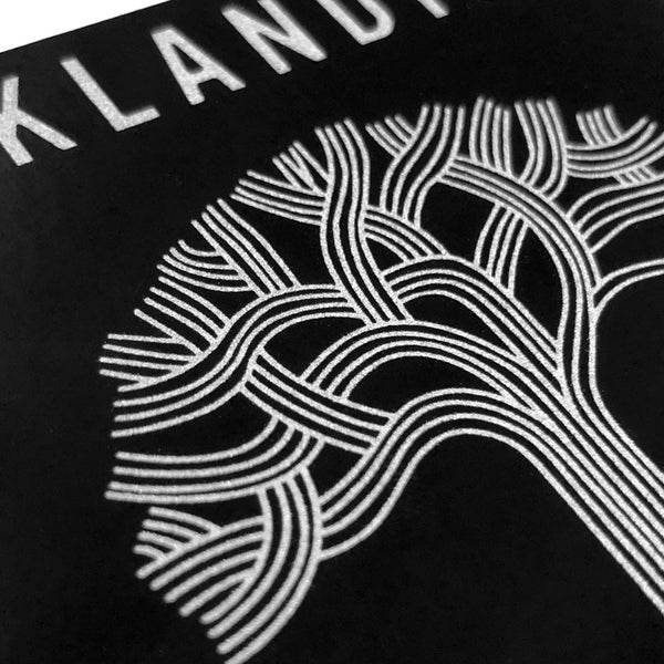 Detailed close-up of silver Oaklandish tree logo on a black rectangular sticker.