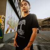 Female model wearing black t-shirt with a large white Oaklandish tree logo on the chest.
