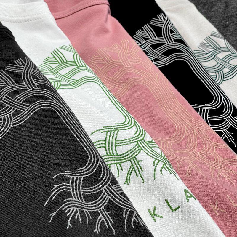 Five colorways of Oaklandish classic tree logo women’s t-shirts (pink, black, heather, white and grey) folded one beside the other.