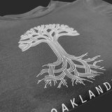 Close up of Oaklandish tree and wordmark logos on folded coal grey scoop neck t-shirt.