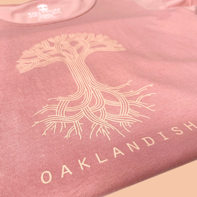 Close up of Oaklandish tree and wordmark logos on folded rose pink scoop neck t-shirt.